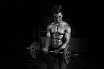 Shirtless male bodybuilder lifting barbell in a dark gym, emphasizing muscles. HD wallpaper