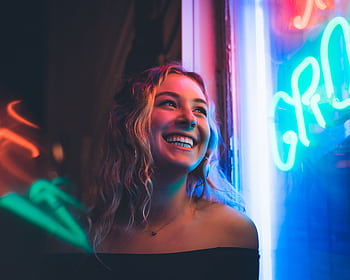 Portrait of a smiling woman with neon lights illuminating her face, capturing a vibrant nighttime atmosphere. HD wallpaper