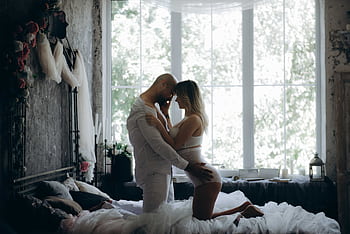 A couple shares an intimate moment in a chic, sunlit bedroom with vintage decor. HD wallpaper