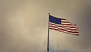 US flag waving in wind against a cloudy sky, symbolizing dom and patriotism. HD wallpaper