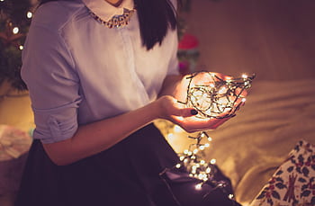 A woman gently cradles a glowing string of Christmas lights in a cozy indoor setting. HD wallpaper