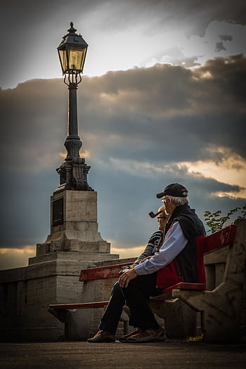 Seniors enjoying a quiet moment on a park bench during a serene sunset. HD phone wallpaper