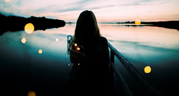 A woman holding lights, silhouetted against a serene lake at twilight. HD wallpaper