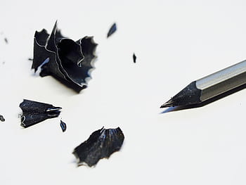 Close-up of a sharpened pencil with black shavings on a white background, ideal for creativity and office themes. HD wallpaper