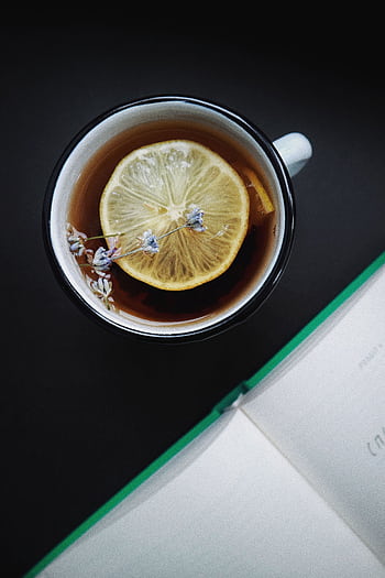 A close-up view of a lemon herbal tea with lavender flowers and an open book in the background. Perfect cozy moment indoors. HD phone wallpaper