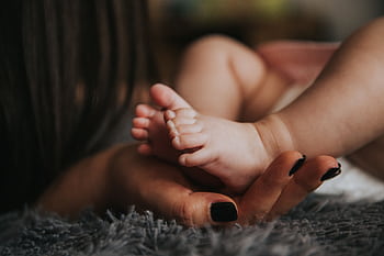 Close-up of a mother's hand gently holding her baby's tiny feet, symbolizing warmth and affection. HD wallpaper