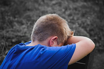 A young boy in a blue shirt rests his head on his arms outdoors, appearing sad and contemplative. HD wallpaper
