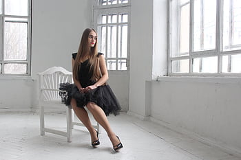 A young woman in an elegant black dress poses in a bright room with large windows, showcasing beauty and style. HD wallpaper