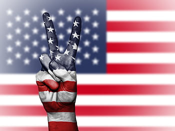 A peace sign hand painted with American flag colors against a blurred US flag backdrop symbolizing patriotism. HD wallpaper