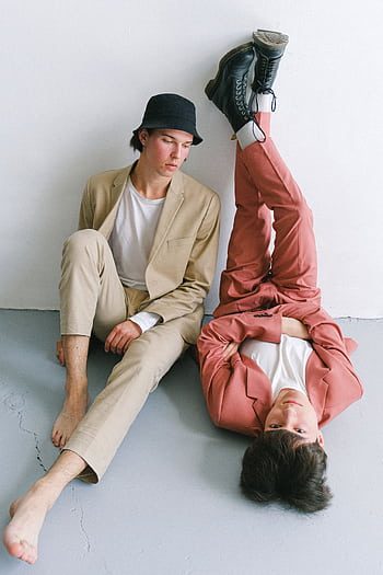 Two young men in stylish suits posing creatively against a white wall. HD phone wallpaper