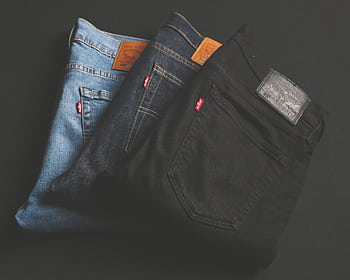 A stack of blue, dark, and black denim jeans folded on a dark surface. HD wallpaper