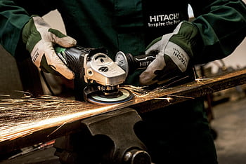 A skilled worker using an angle grinder on metal, producing sparks in an industrial workshop. HD wallpaper