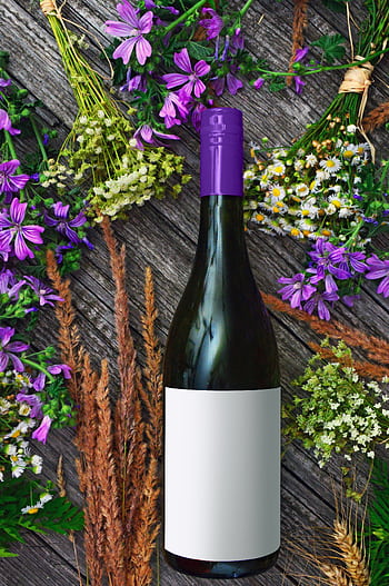 A wine bottle surrounded by vibrant purple flowers and greenery on a rustic wooden surface. HD phone wallpaper