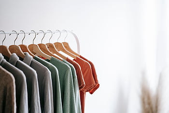 Neatly organized clothes on wooden hangers on a minimalist rack in a bright room. HD wallpaper