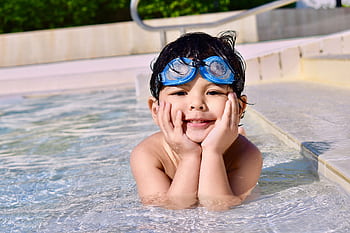 A young child with goggles smiling while playing in an outdoor swimming pool. HD wallpaper