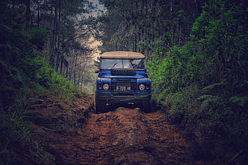 Off-road vehicle traversing a rugged dirt path through lush forest in Parongpong, Indonesia. HD wallpaper