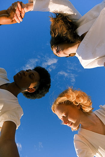 Three women holding hands under a clear blue sky, symbolizing unity and friendship. HD phone wallpaper
