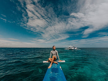 Man sitting on a boat's bow, enjoying a peaceful ocean view under a blue sky. HD wallpaper