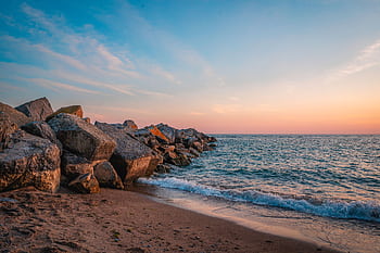 A serene sunset view over the rocky beach in Toronto, Canada. Waves gently crash against the shore. HD wallpaper