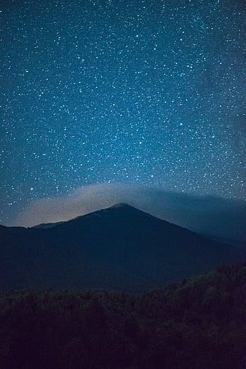 A mesmerizing view of a star-filled night sky over a silhouetted mountain, perfect for serene . HD phone wallpaper