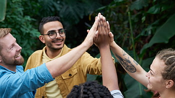 A joyful group of friends high-fiving outdoors, symbolizing teamwork and camaraderie. HD wallpaper