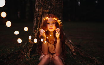 A young girl with fairy lights creates a magical evening mood outdoors. HD wallpaper