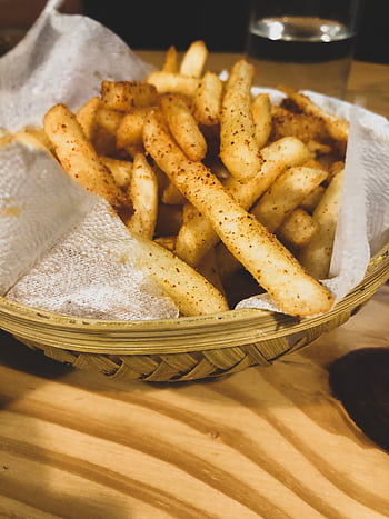 Close-up of seasoned french fries served in a rustic basket on a wooden table. HD phone wallpaper