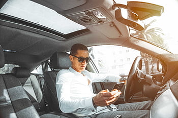 A man wearing sunglasses texts on his while driving a car in Morocco. HD wallpaper