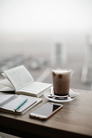 A warm coffee sits beside a notebook and smart on a foggy day. HD phone wallpaper