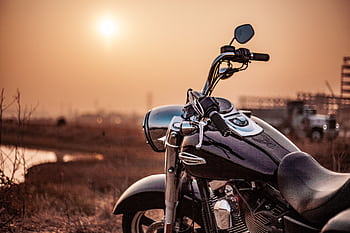 Harley Davidson motorcycle parked outdoors at sunset, capturing the warm glow and serene environment. HD wallpaper