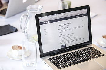 Close-up of a MacBook Pro displaying a webpage, with coffee cups and water pitcher on a table. HD wallpaper