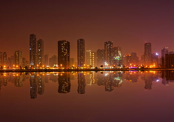 Dramatic cityscape at night with buildings reflecting in tranquil water. HD wallpaper