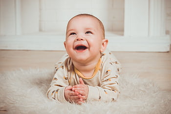 Joyful baby lying on a fluffy rug, smiling and looking upwards indoors. HD wallpaper