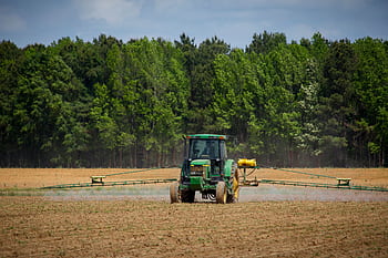 Tractor spraying fields with pesticides on a countryside farm in summer with a forest backdrop. HD wallpaper