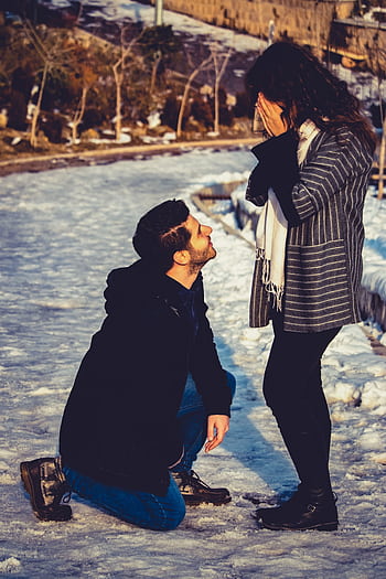 A man proposing to his girlfriend in a snowy park during winter, capturing a heartfelt moment outdoors. HD phone wallpaper