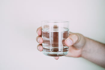 A close-up shot of a hand holding a clear glass of water, symbolizing refreshment. HD wallpaper