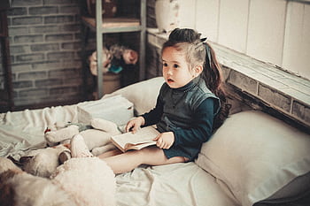 A cute little girl reading a book in a warm and cozy bedroom environment. HD wallpaper