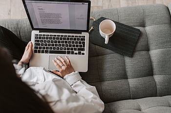 Woman working remotely on a laptop while relaxing on a cozy sofa at home. HD wallpaper