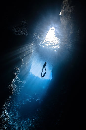 A breathtaking view of a scuba diver silhouetted in a sunlit underwater cavern. HD phone wallpaper