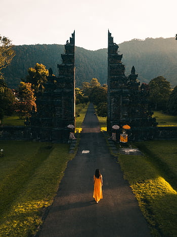 Aerial view of a woman in orange dress walking towards Bali Handara Gate at sunrise in Indonesia. HD phone wallpaper
