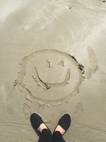 A smiley face drawn in sand on a sunny beach, captured with shoes visible. HD phone wallpaper