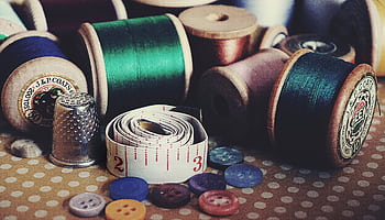 Close-up of vintage sewing essentials including threads, buttons, thimble, and measuring tape. HD wallpaper
