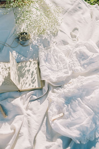 Elegant picnic setup with book, delicate flowers, and soft white textiles in sunlight. HD phone wallpaper