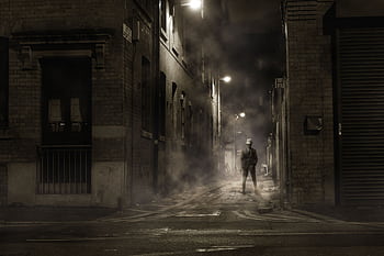 A lone figure in a foggy, dimly lit alley creates a mysterious noir atmosphere. HD wallpaper