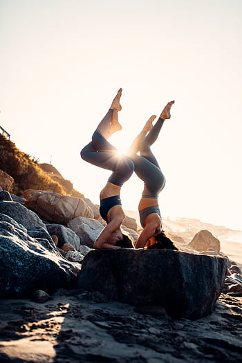 Two women performing acro yoga on rocks during sunset in Malibu, showcasing balance and flexibility. HD phone wallpaper