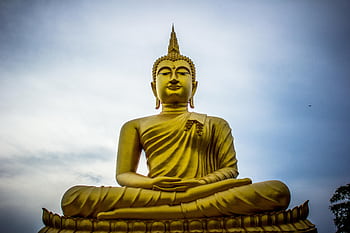 A majestic golden Buddha statue against a serene blue sky, symbolizing peace and spirituality. HD wallpaper