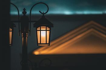 A warm, illuminated street lamp against a soft-focus architectural background creates a captivating night scene. HD wallpaper