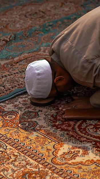 Man in traditional attire praying on a beautiful Persian carpet indoors, showcasing Islamic spirituality. HD phone wallpaper