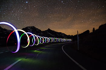 Enchanting long exposure of colorful light trails on a winding road beneath a star-filled sky. HD wallpaper
