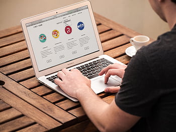 Person typing on laptop outdoors, illustrating remote work lifestyle with coffee at a wooden table. HD wallpaper